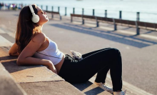 woman sitting on a bench overlooking the beach wearing white headphones