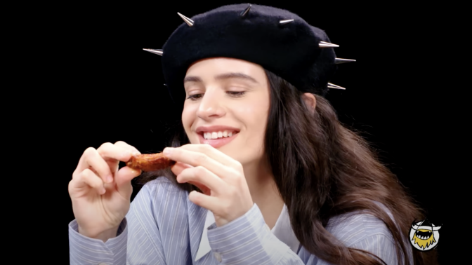 The singer Rosalia holds a chicken wing on "Hot Ones"